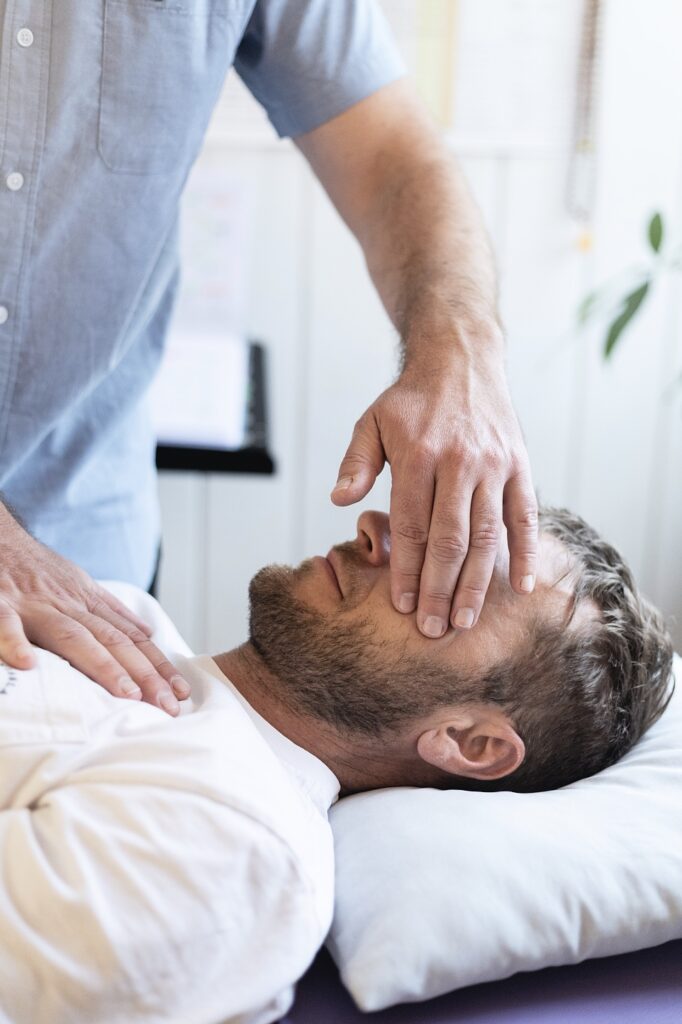 Man lying on his back as a caregiver checks his breathing or provides first aid by placing a hand near his face/torso.