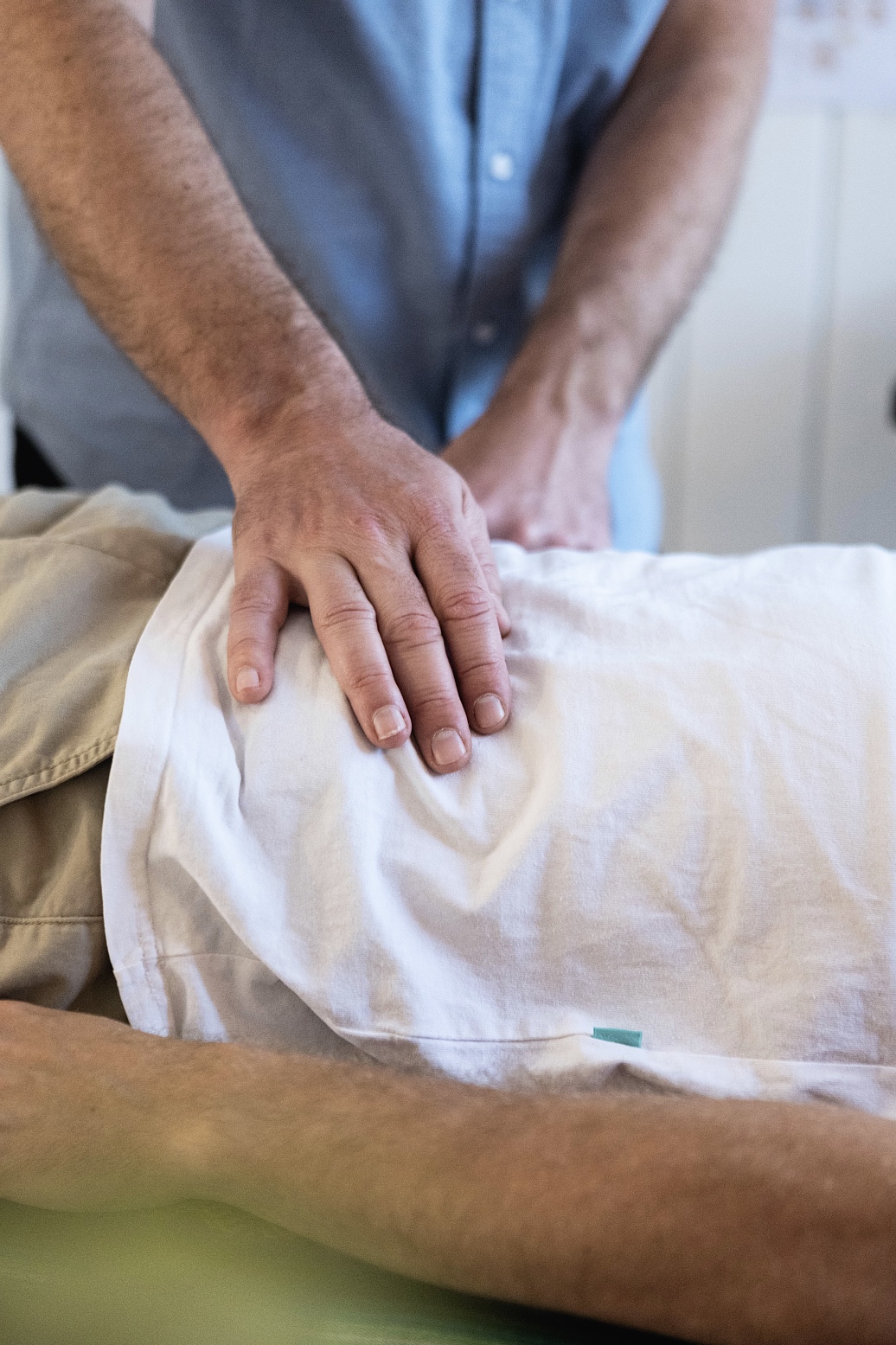 Caregiver placing a hand on a patient’s back while the patient lies on a bed or examination table, suggesting support or examination.