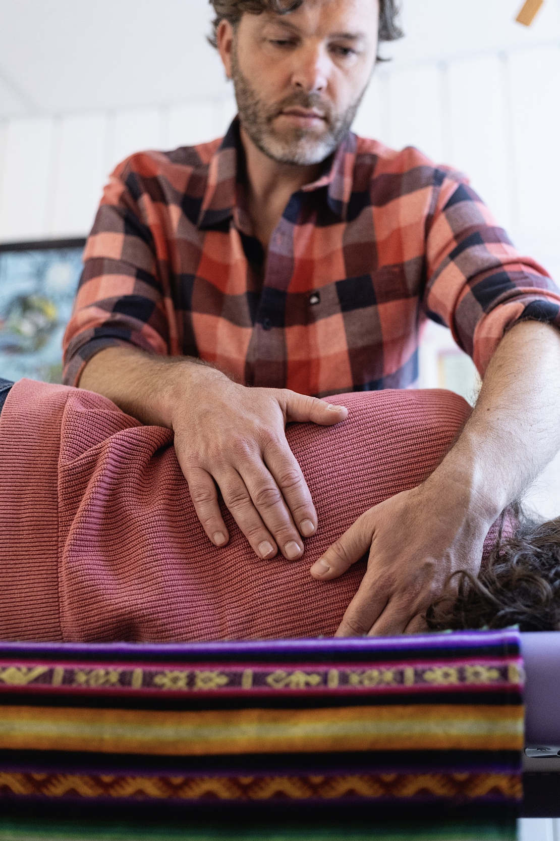 Therapist in a red plaid shirt applies pressure on a person lying face down on a table during a massage or chiropractic session.